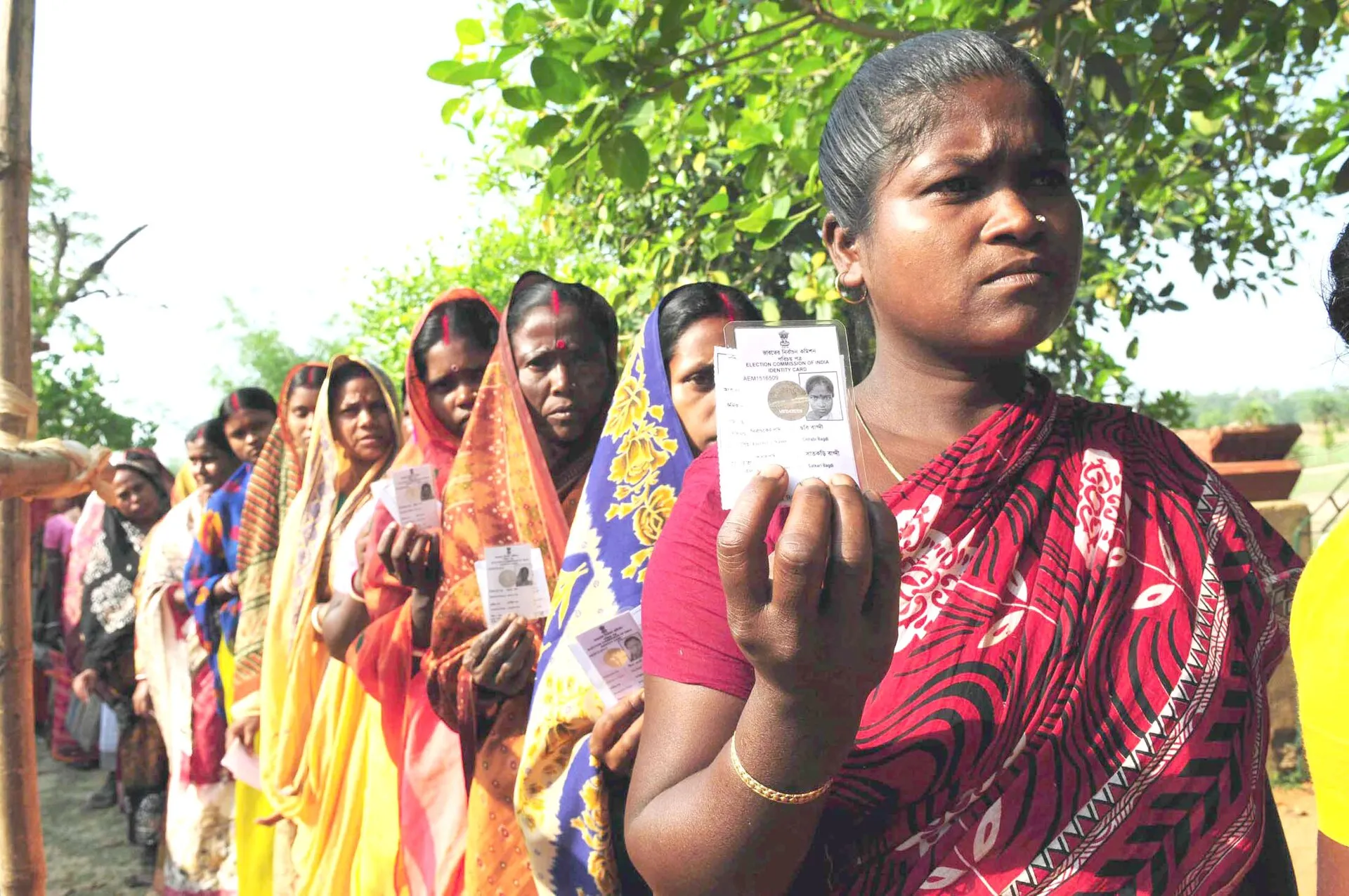 Women voters in a queue at a village polling station in West Bengal, one holding up her voter identity card (2011 Assembly election)