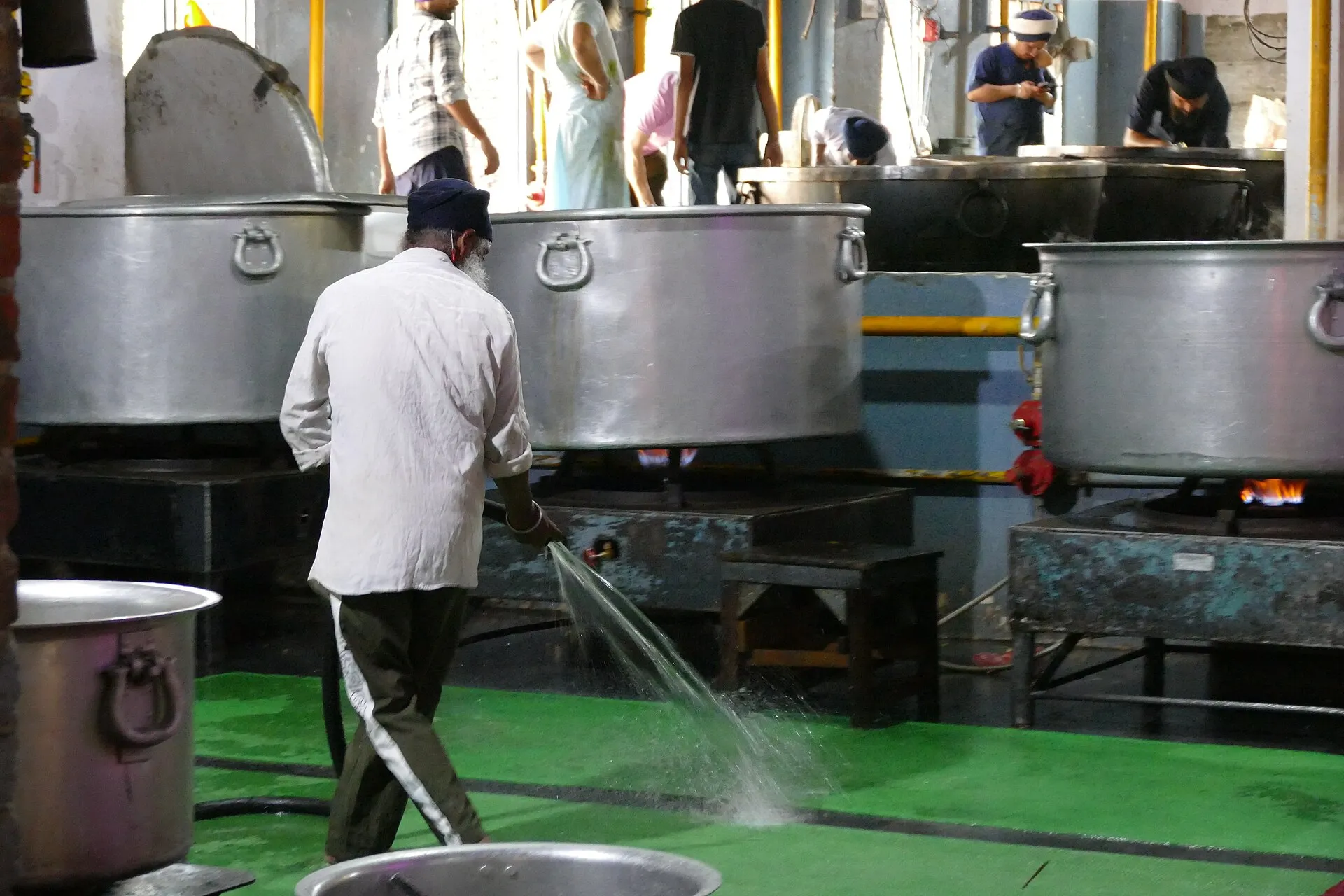 A sevadar hosing down the floor beside giant cooking pots in the Guru Ram Das Langar kitchen at the Golden Temple