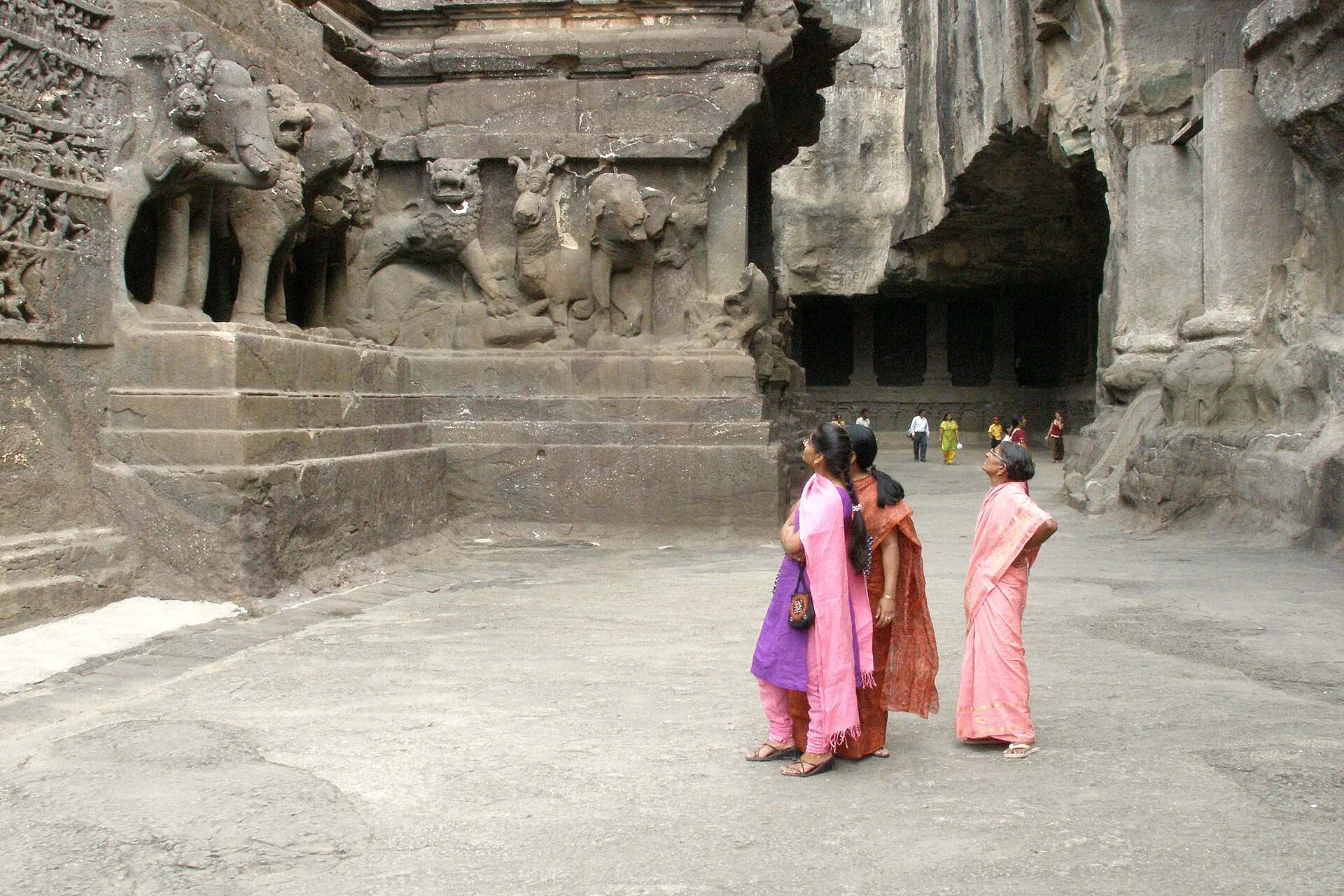 Visitors in saris standing in the courtyard of the Kailasa Temple at Ellora, beside a carved stone elephant and rock-cut walls