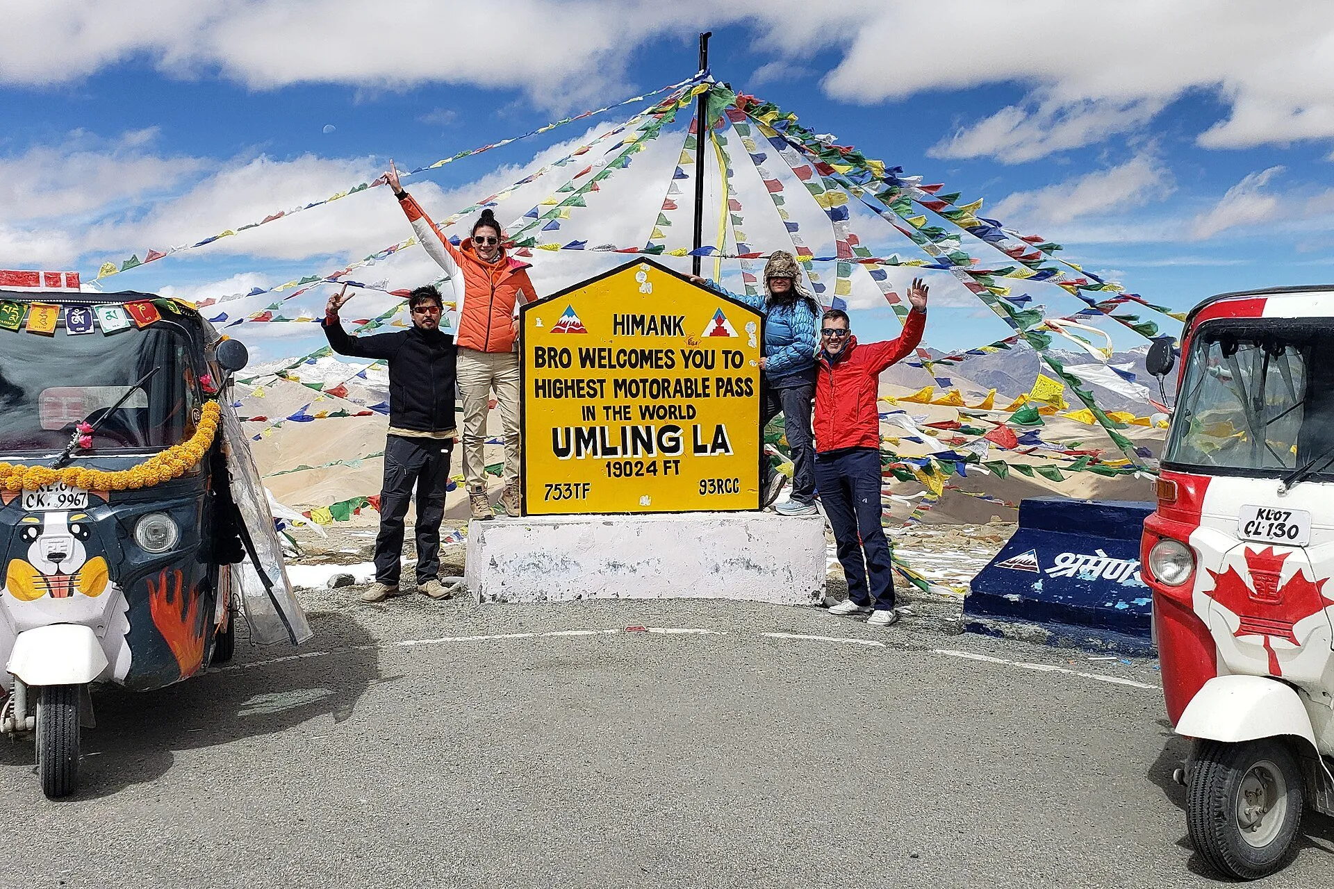Travellers at the summit sign of Umling La, the earlier record-holder for the highest motorable pass, with prayer flags behind