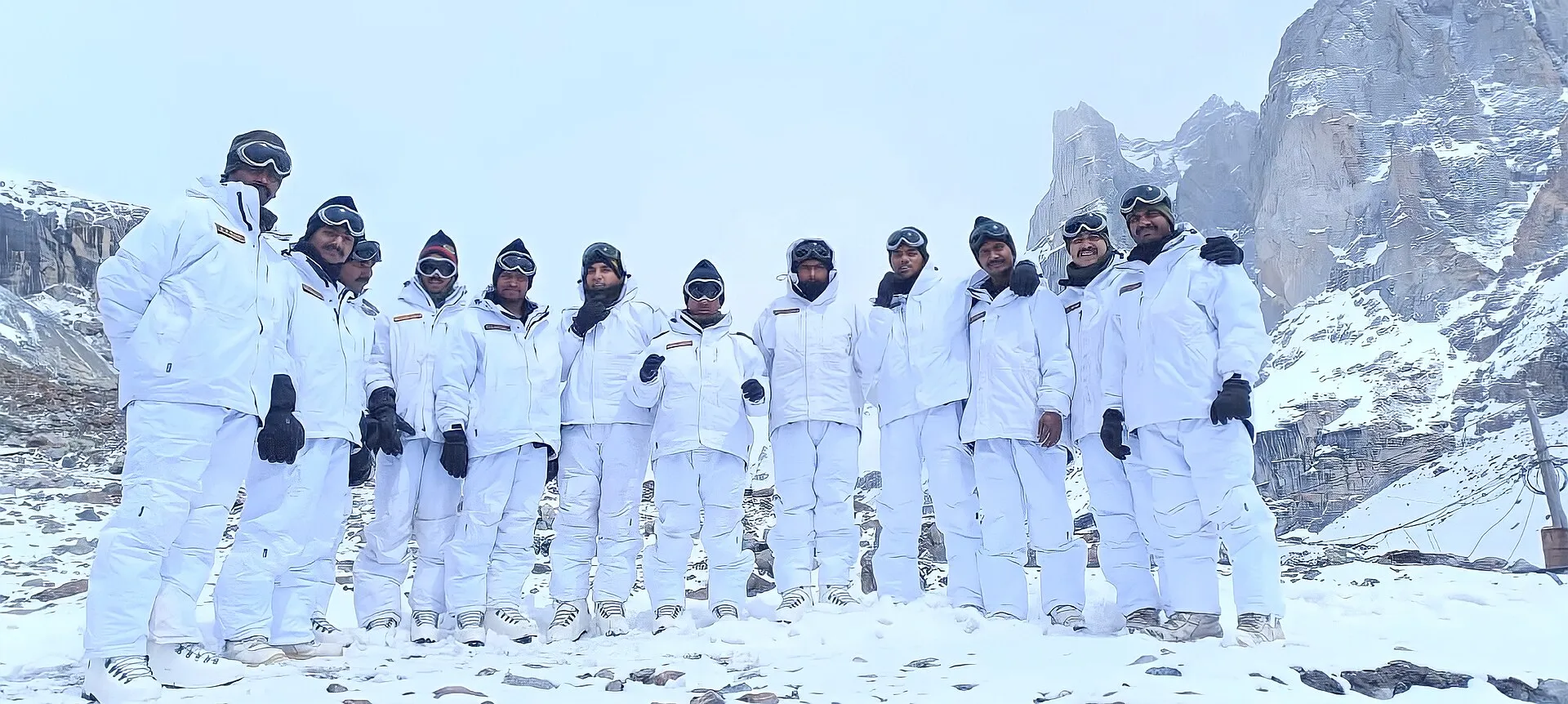 A line of Indian soldiers in white snow gear standing on a snowfield below jagged peaks in the Siachen region